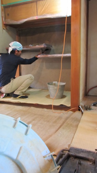 Can you appreciate how tricky this cubby must be to plaster? Going around that shelving... Here, Maru-san is making sure he can take enough time to hit all the details without loosing moisture, using a small brush to wet down each little edge. As a tarp he is using a "mushiro," the stripped off surface of a tatami mat that we can get from tatami refinishers. Reused! It's our standard tarp indoors. Also note he is wearing "inside shoes." We have to change our shoes at the entrance, as per Japanese custom.